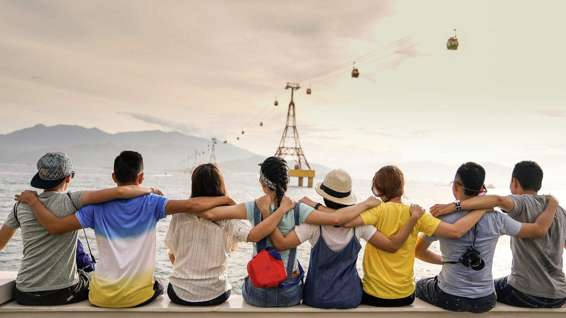 Friends sitting together beside the water, with their arms around one another